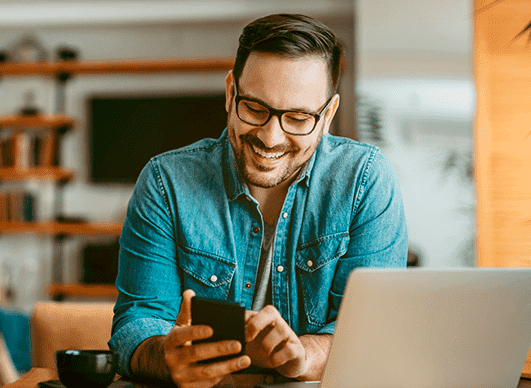 Homem olha para a tela do celular e sorri.