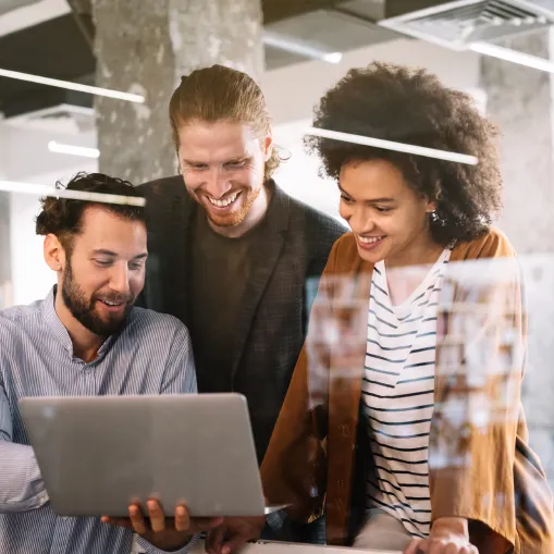 Dois homens e uma mulher trabalham em computador e sorriem