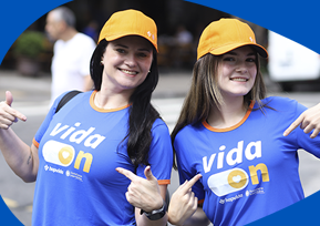 Duas mulheres estão sorrindo e apontando para suas camisetas azuis com o logo 