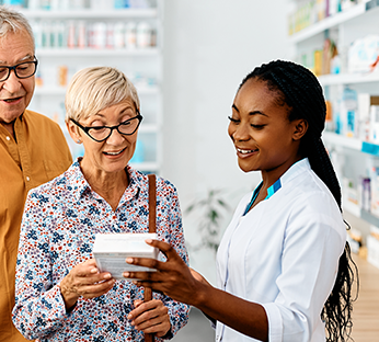 Farmacêutica sorridente explicando informações sobre um produto a dois clientes idosos em um ambiente de farmácia.